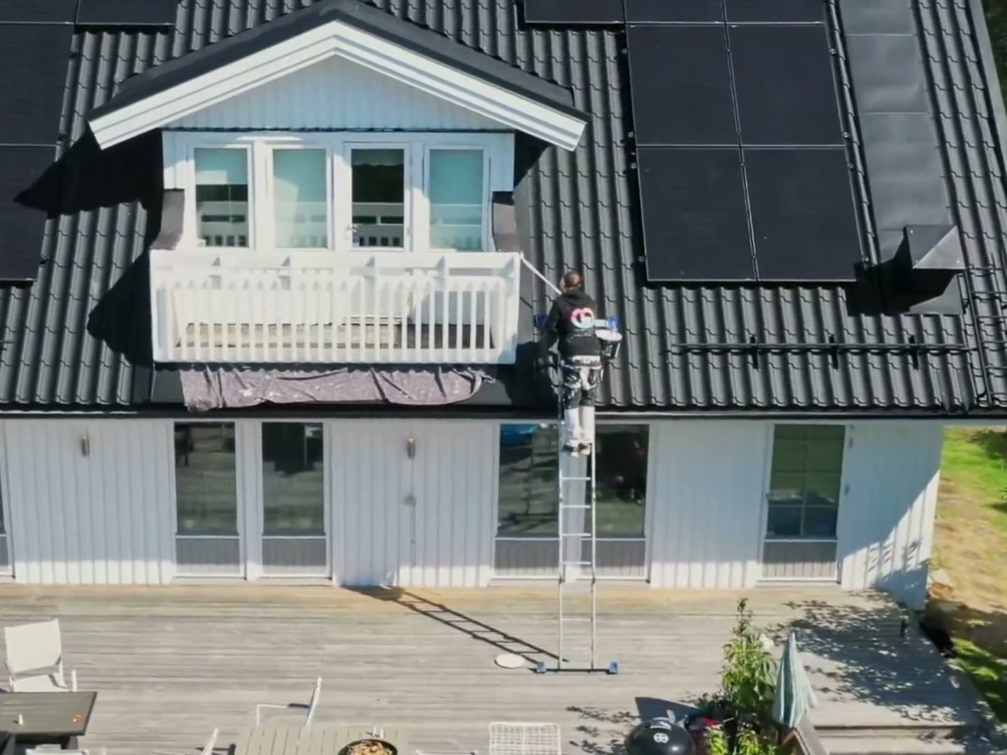 En målare på stege målar vid balkongen på ett vitt hus, sett uppifrån, ur GD Måleris egen film
