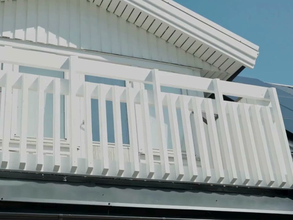 Vitmålad vindskiva och balkongräcke på en vit villa mot blå himmel, bildruta ur GD Måleris egen film