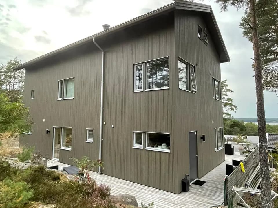 Nymålad grå träfasad på ett modernt tvåvåningshus i Täby kyrkby, sedd från tomten