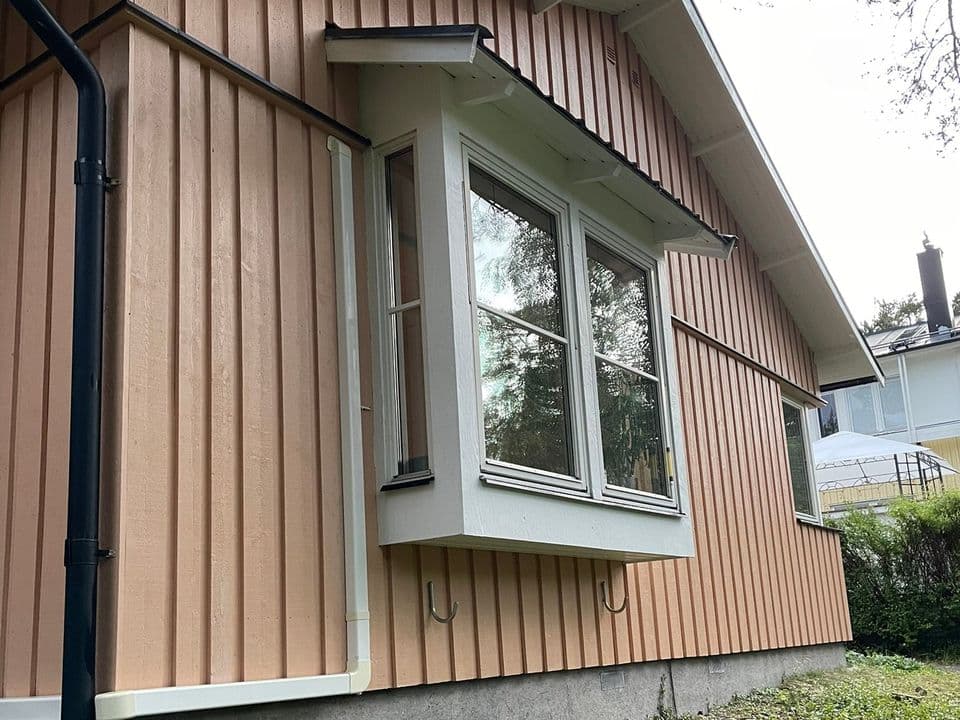 Nymålad laxrosa panelfasad med vitt burspråksfönster och svart stuprör